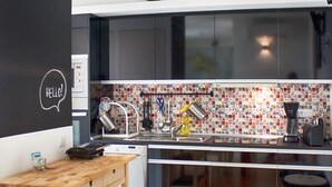 A modern kitchen with a wooden table and chairs, a coffee machine, and a colorful backsplash.