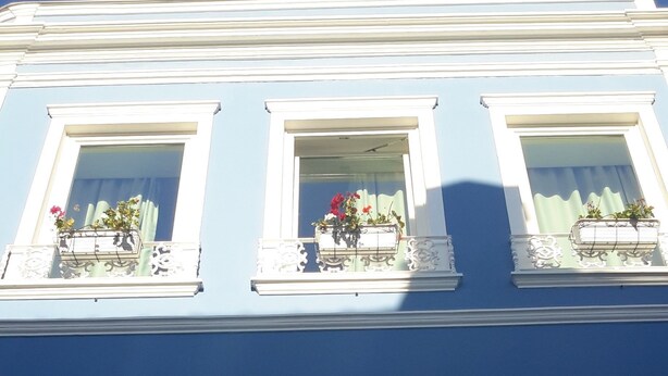 A building with three windows, each with a balcony. The balconies have ornate white railings and are adorned with flower boxes.