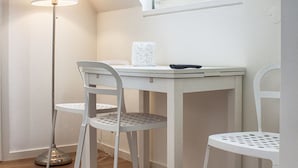A small, white room with a sloped ceiling, a desk, two chairs, a floor lamp, and a window.