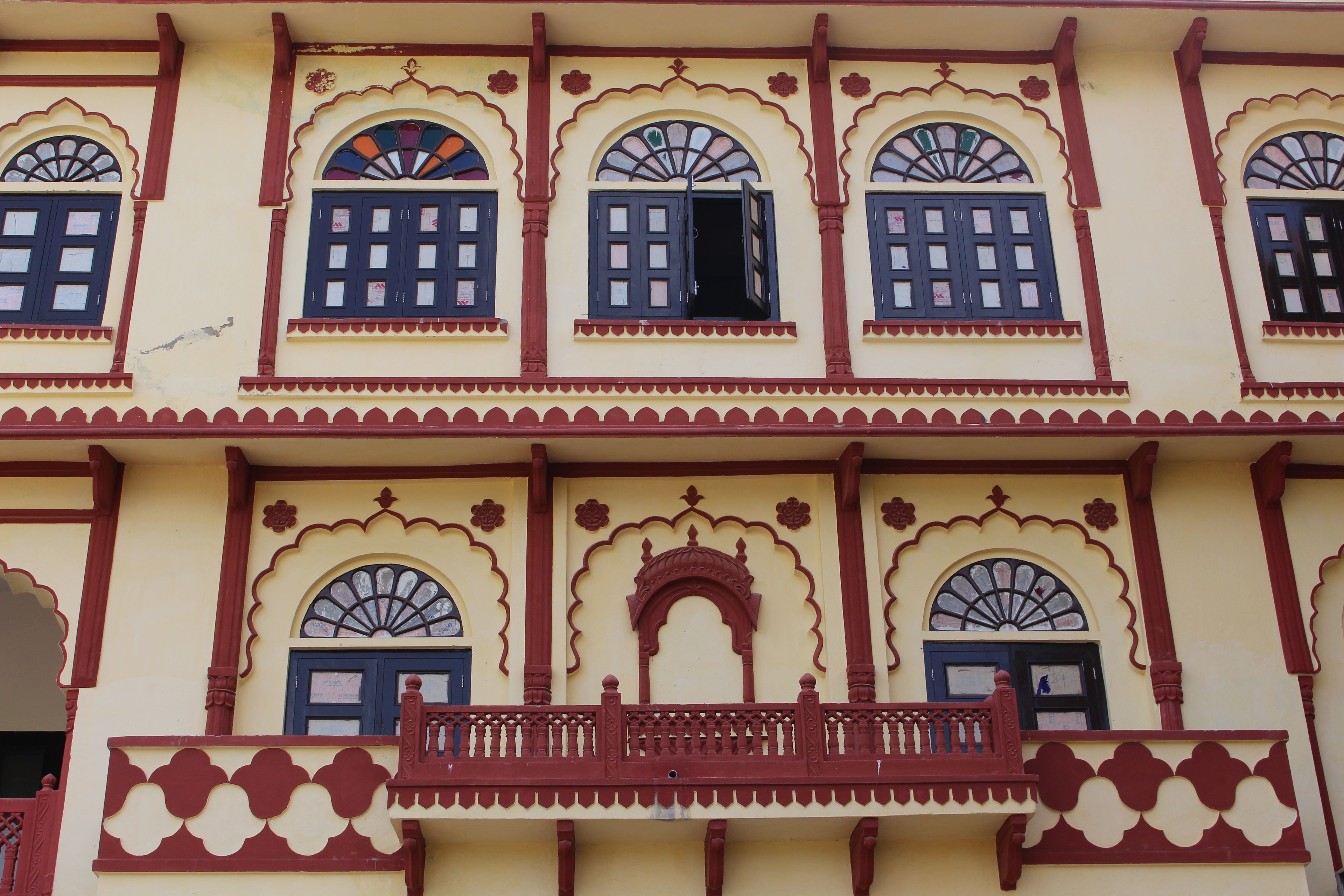 A building with multiple windows, some with open shutters, and a balcony with a railing.