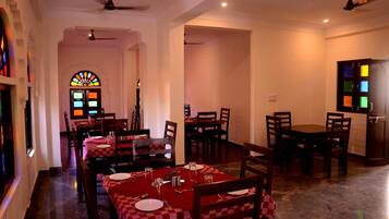 A dining area with tables set for four, each with red and white checkered tablecloths, and a stained glass window in the background.