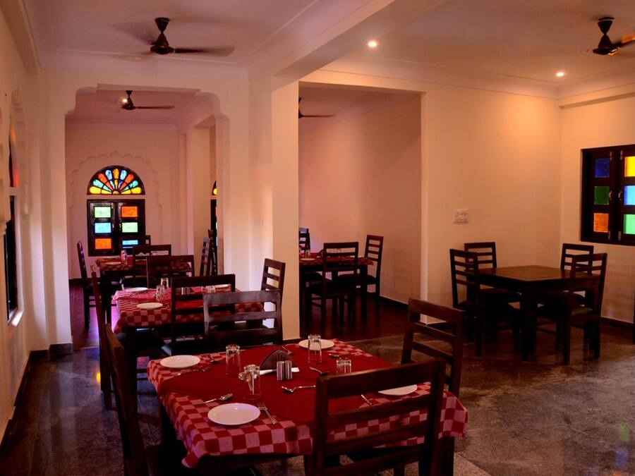 A dining area with tables set for four, each with red and white checkered tablecloths, and a stained glass window in the background.