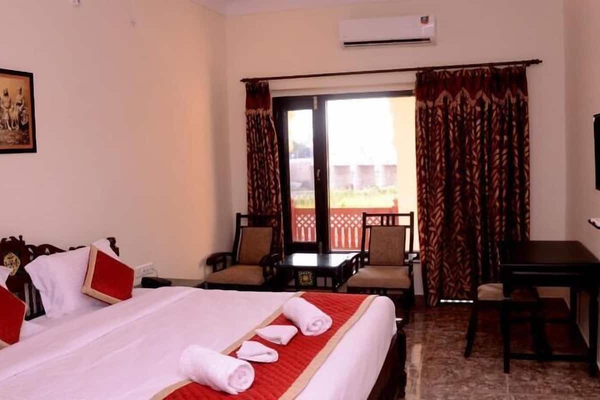 Quarto de hotel com cama, escrivaninha, cadeira e televisão.