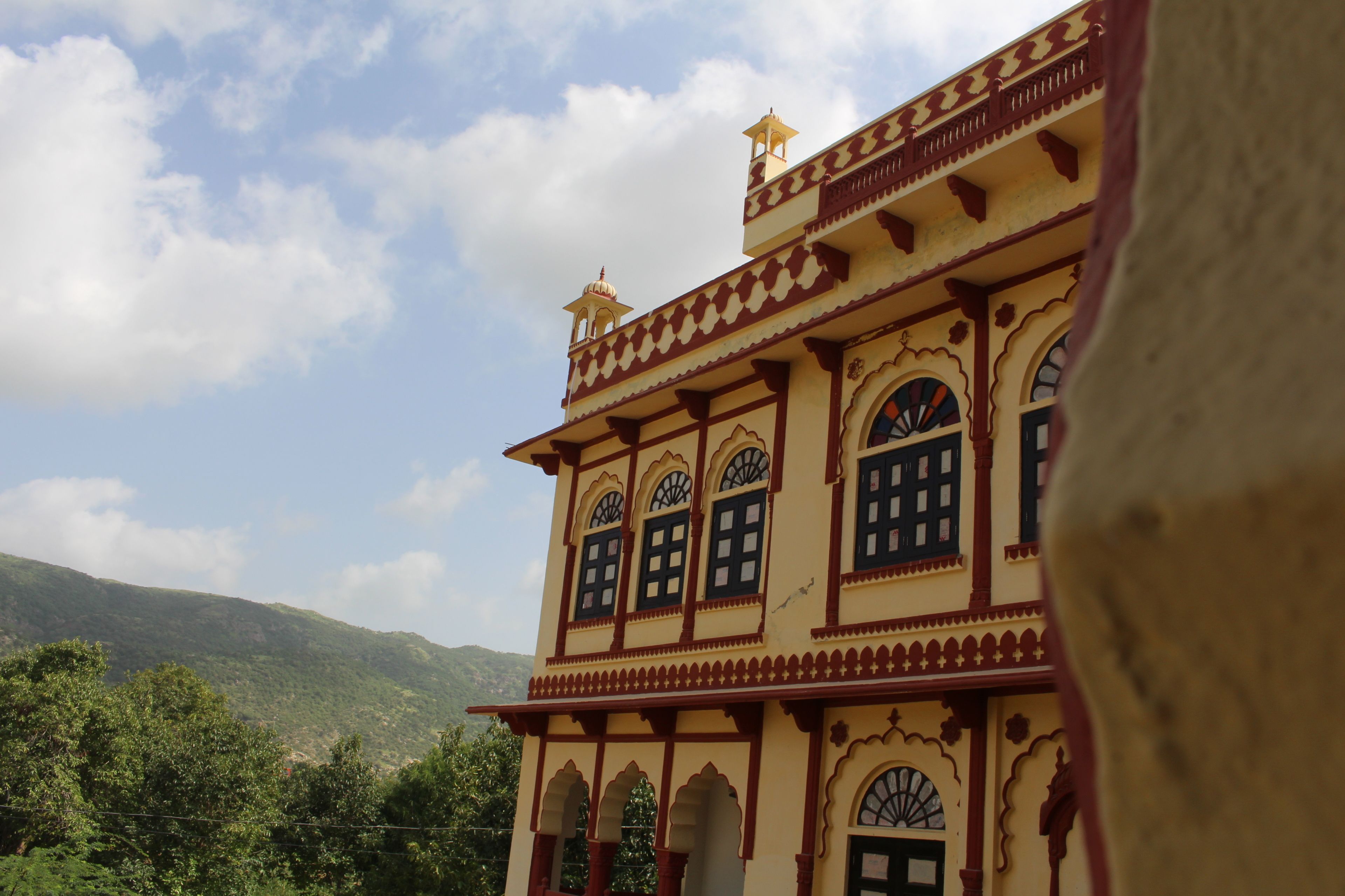 A traditional building with arched windows and decorative elements, set against a mountainous backdrop.