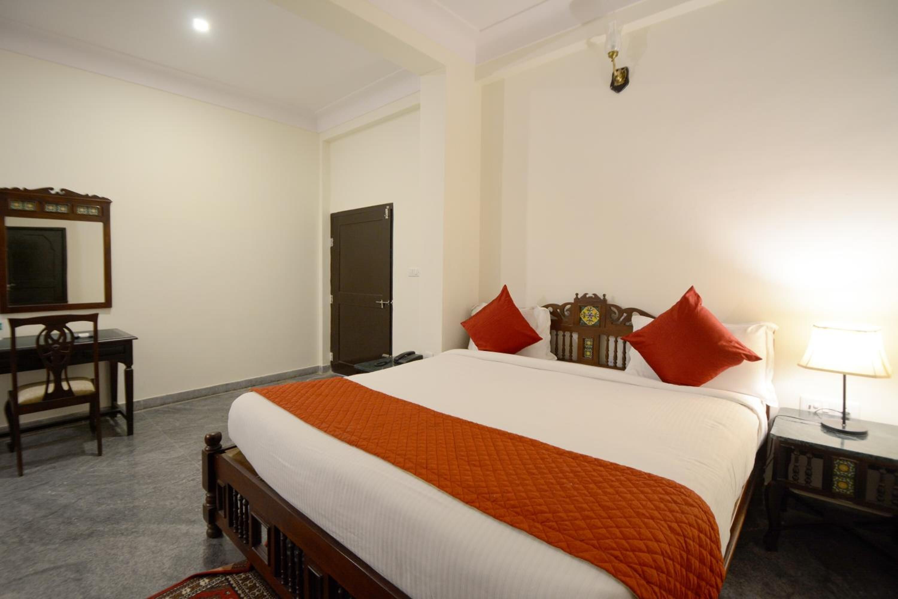 A hotel room with a large bed, a desk, a chair, a wardrobe, and a bedside table with a lamp.