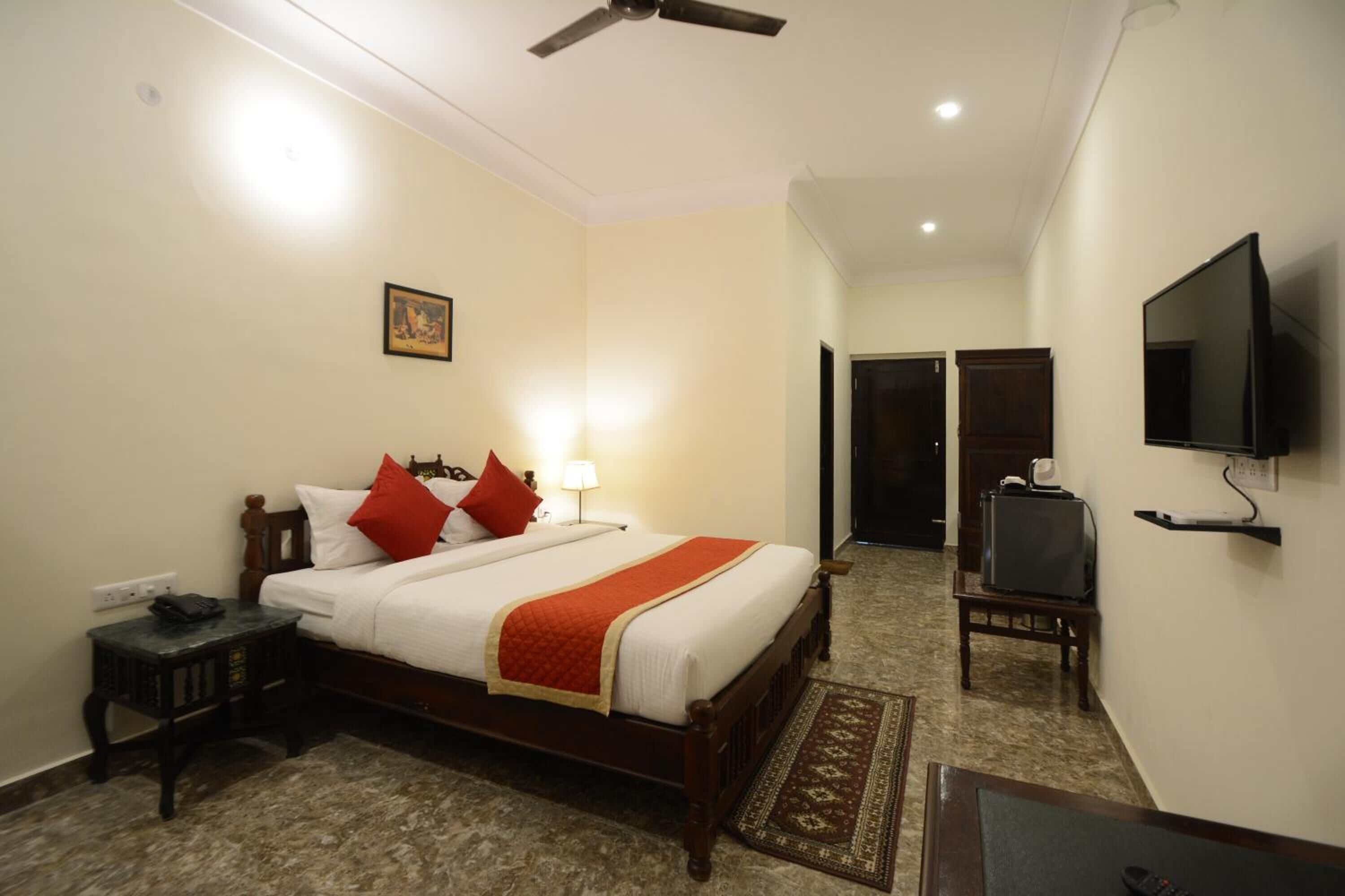 A hotel room with a bed, bedside table, lamp, TV, and a ceiling fan.