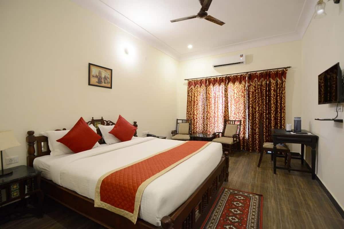 Quarto de hotel com uma cama grande, escrivaninha, cadeira, televisão e ventoinha no teto.