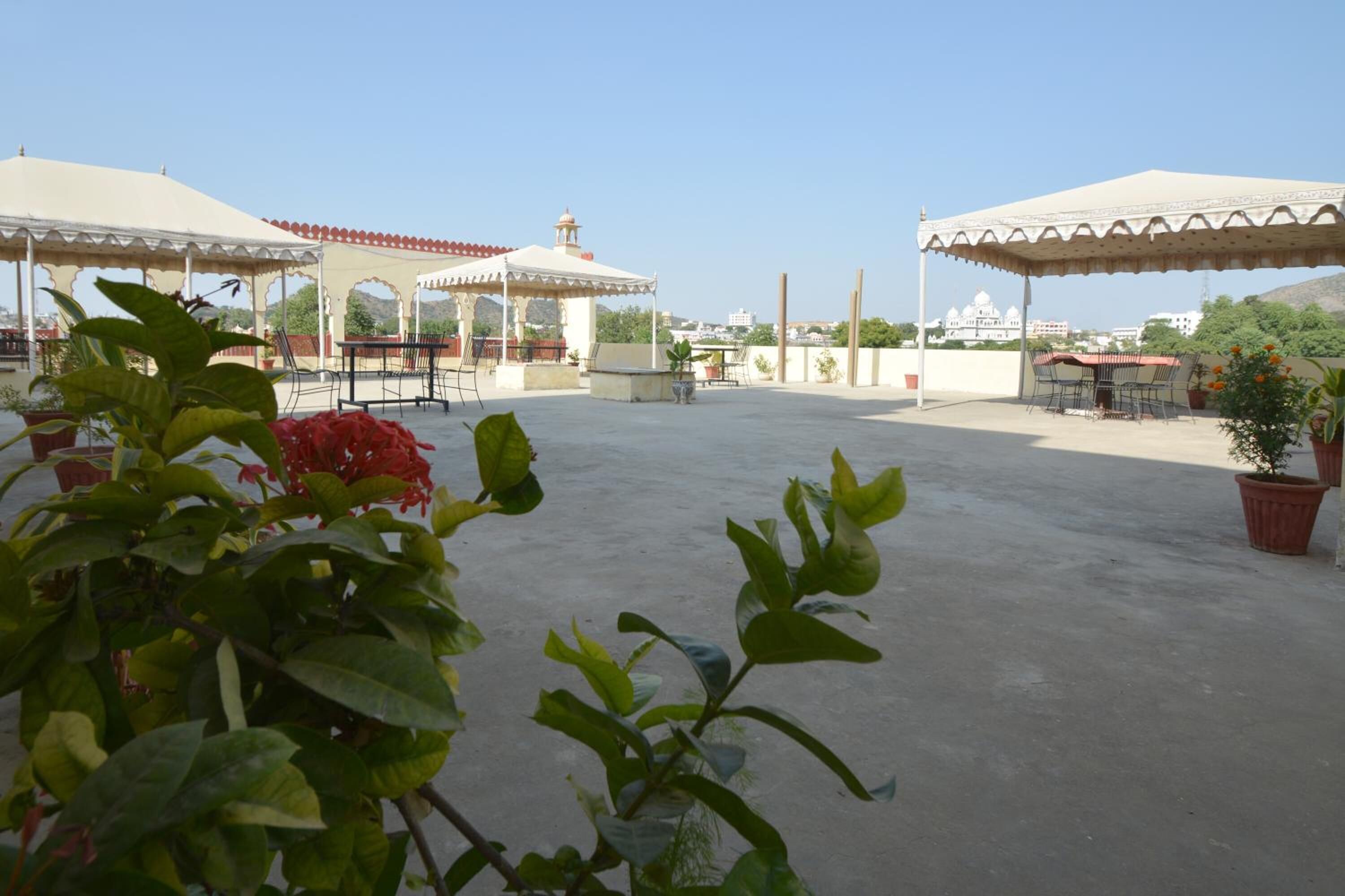 An outdoor terrace with covered seating areas, potted plants, and a view of distant buildings.