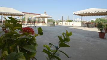 An outdoor terrace with covered seating areas, potted plants, and a view of distant buildings.