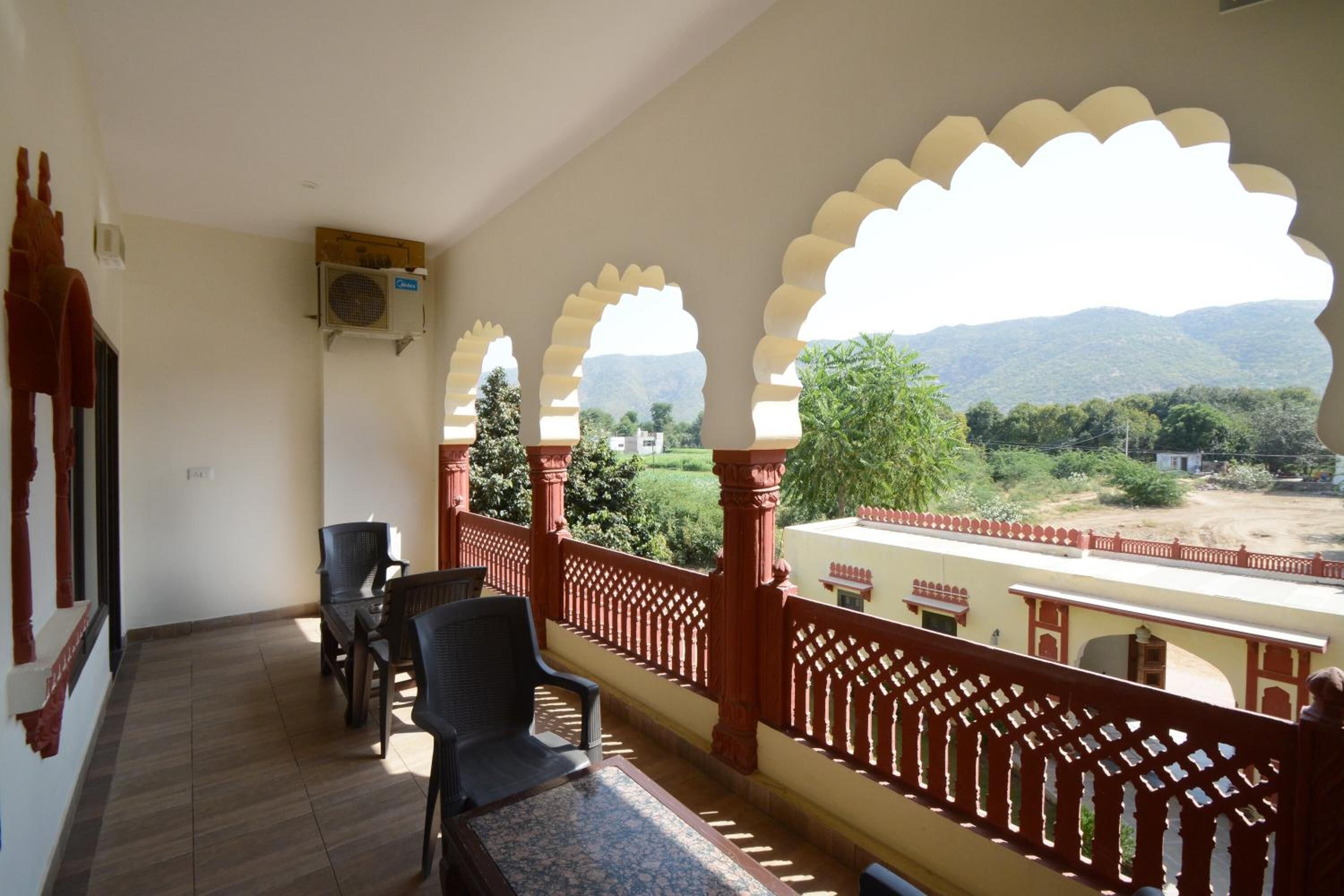 Un balcón con vistas a un paisaje montañoso, un ventilador en la pared y una mesa con sillas.