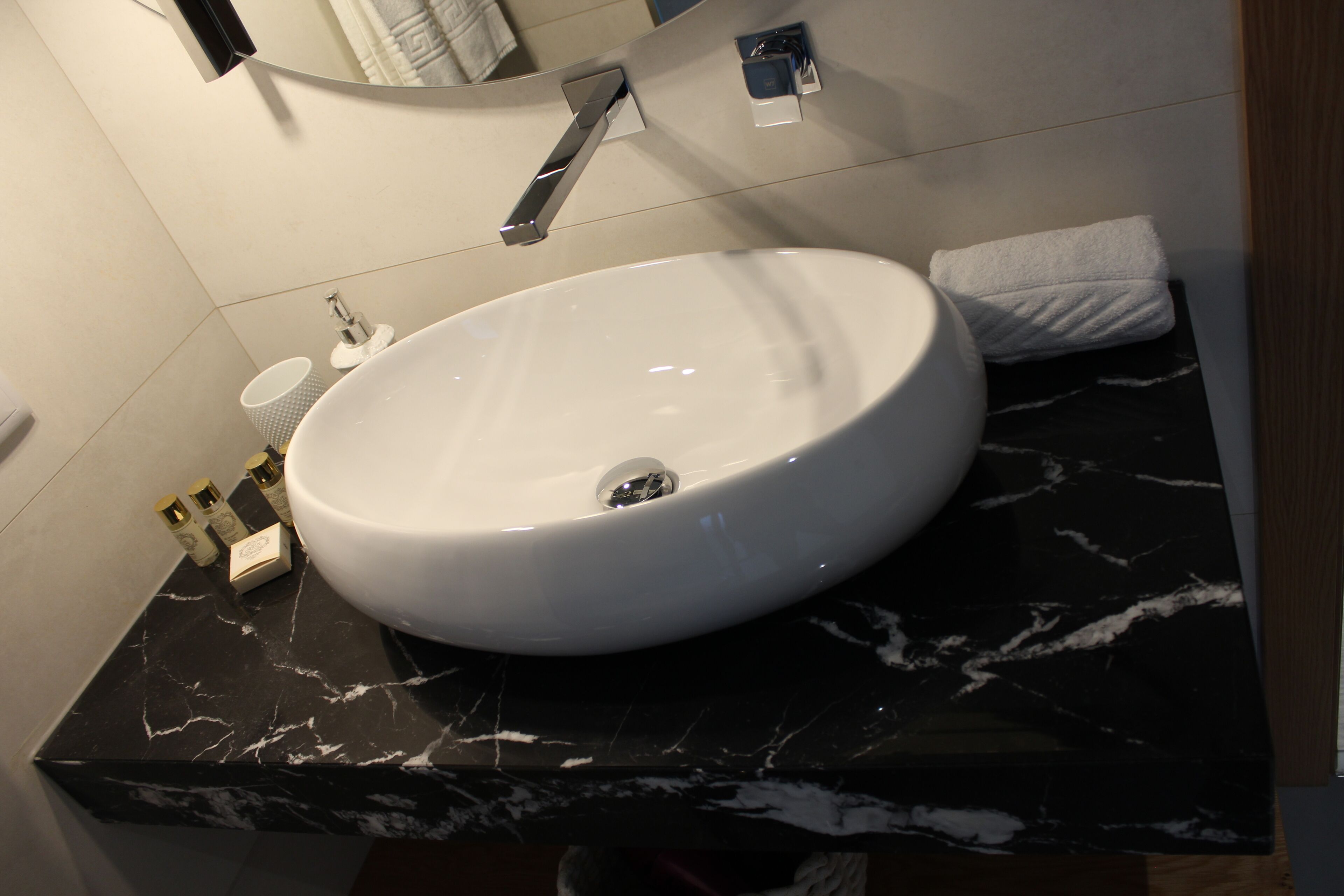 Une salle de bain avec un lavabo blanc, un plan de toilette en marbre noir et un miroir au-dessus du lavabo.