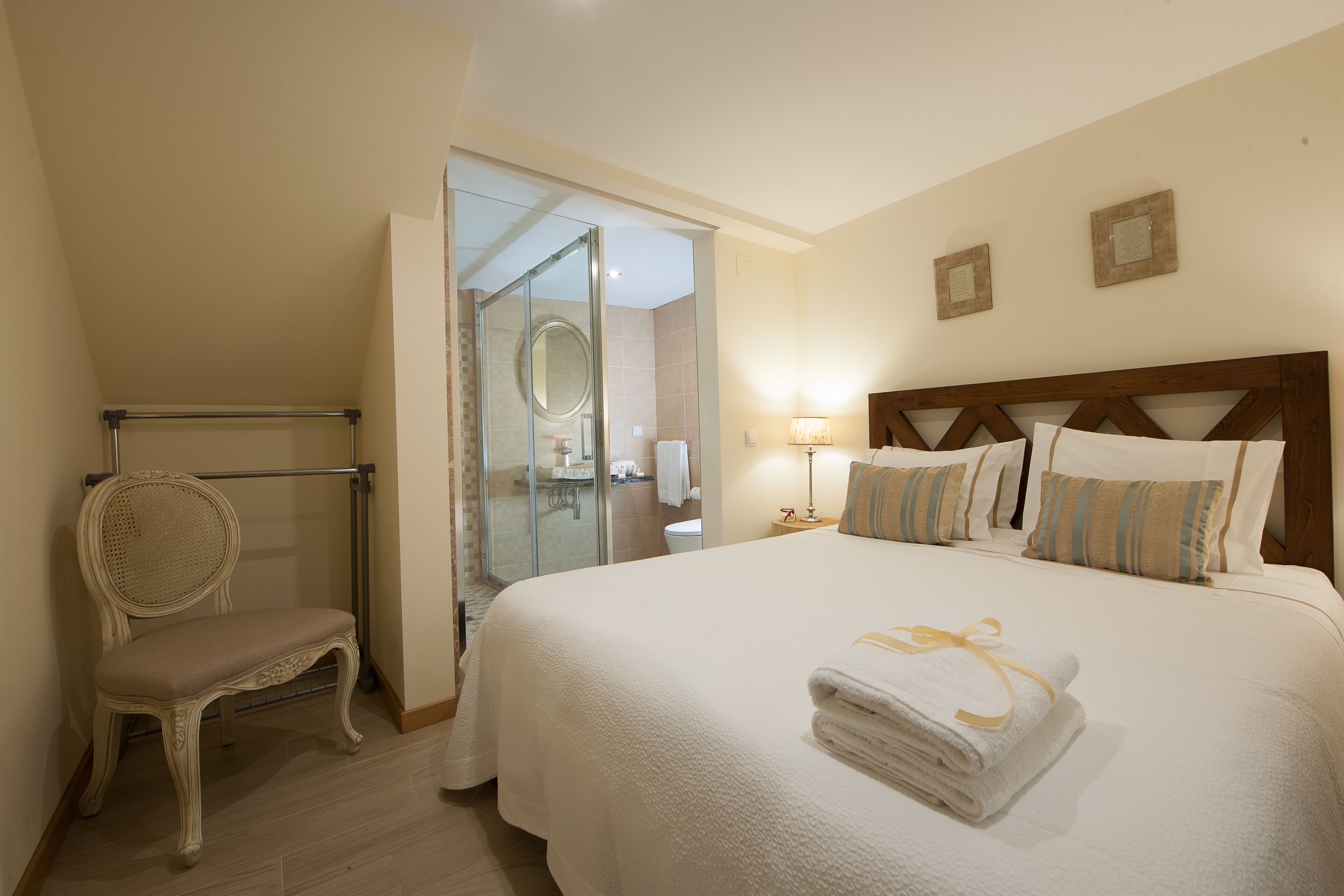 A hotel room with a large bed, a chair, a glass shower enclosure, and a bedside table with a lamp.