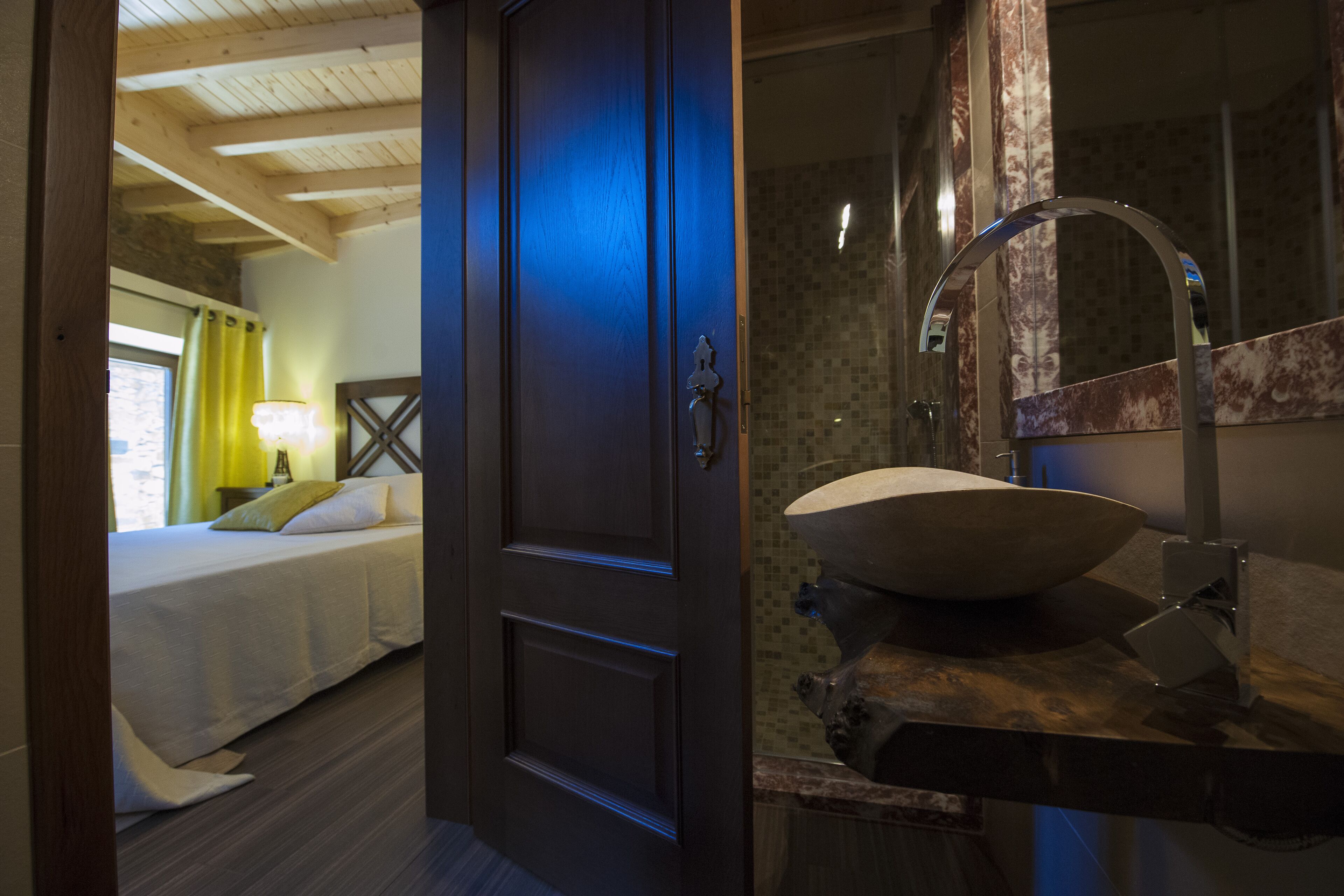 Una habitación de hotel con cama, puerta de madera y baño con lavamanos grande y espejo.