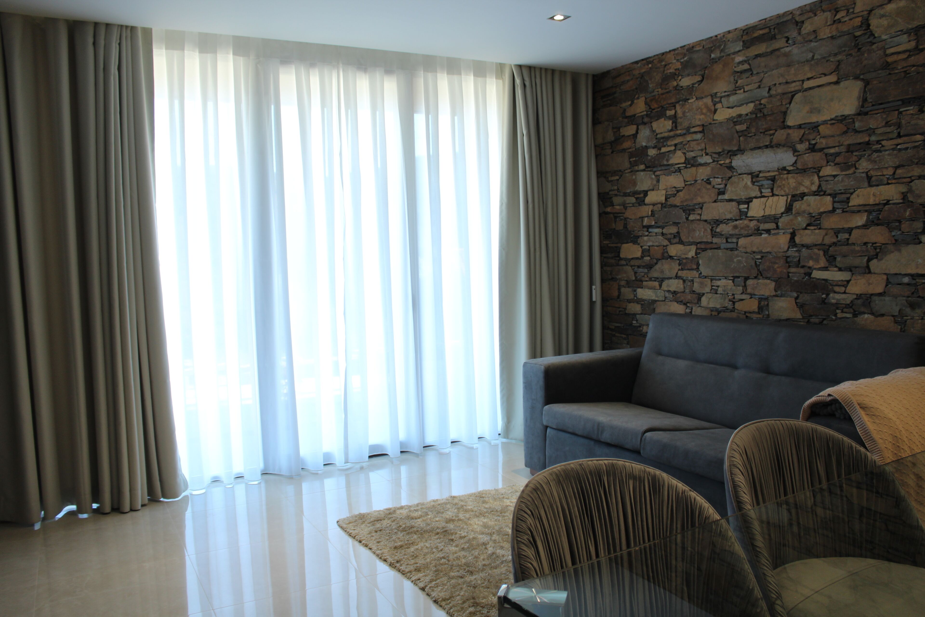 A modern living room with a stone wall, a grey sofa, and a beige rug.