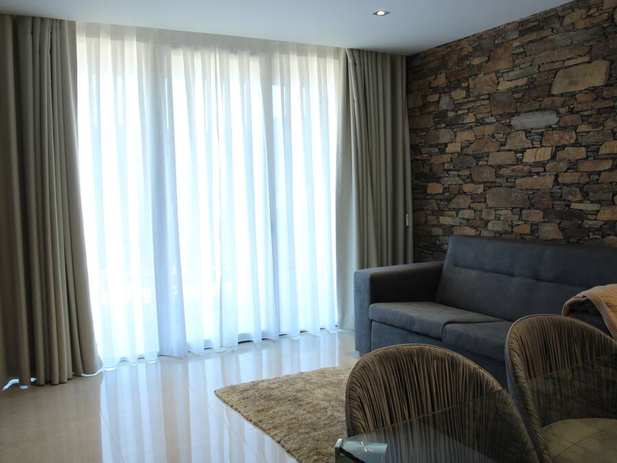 A modern living room with a stone wall, a grey sofa, and a beige rug.
