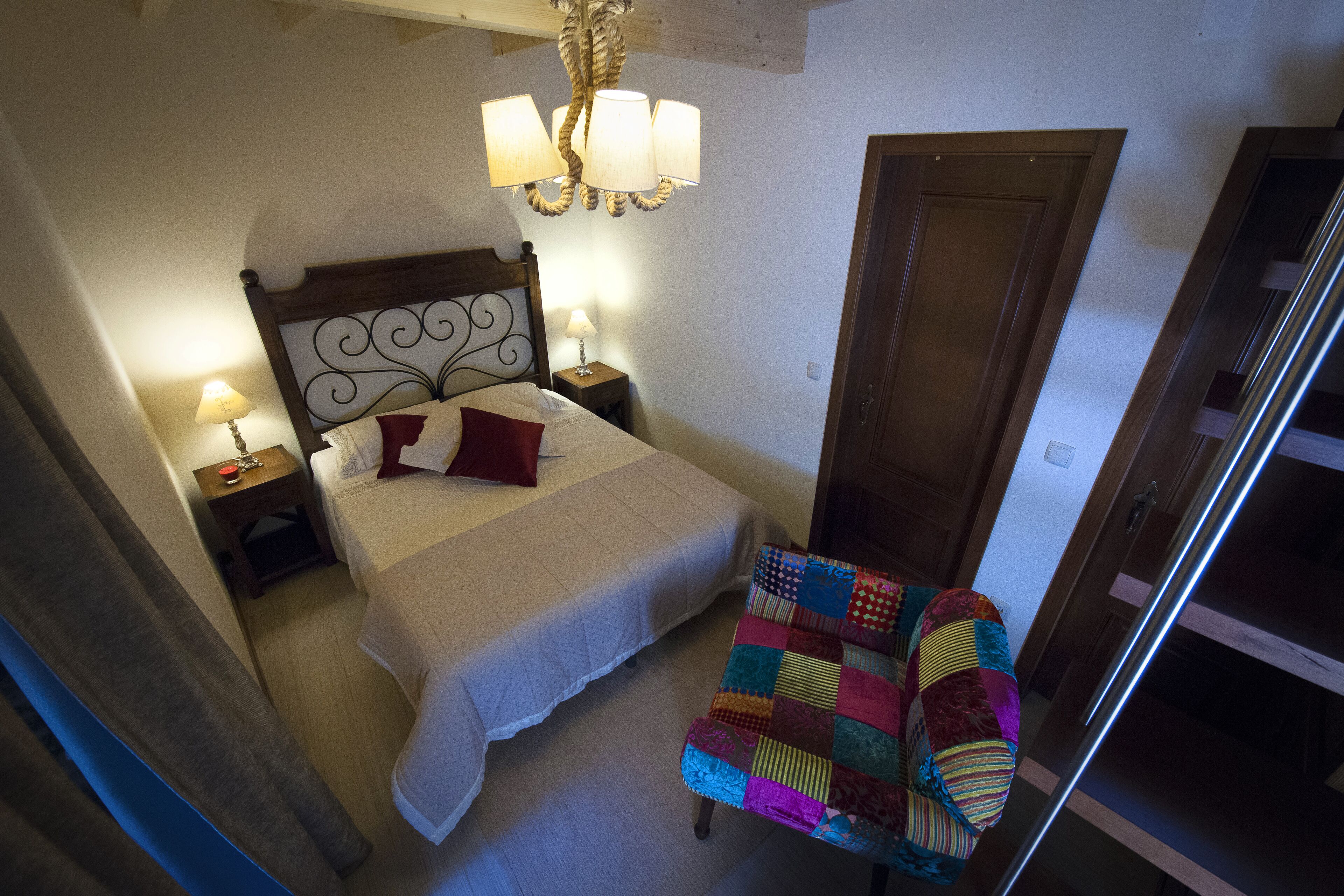 A bedroom with a bed, bedside lamps, a quilted chair, and a wooden door.