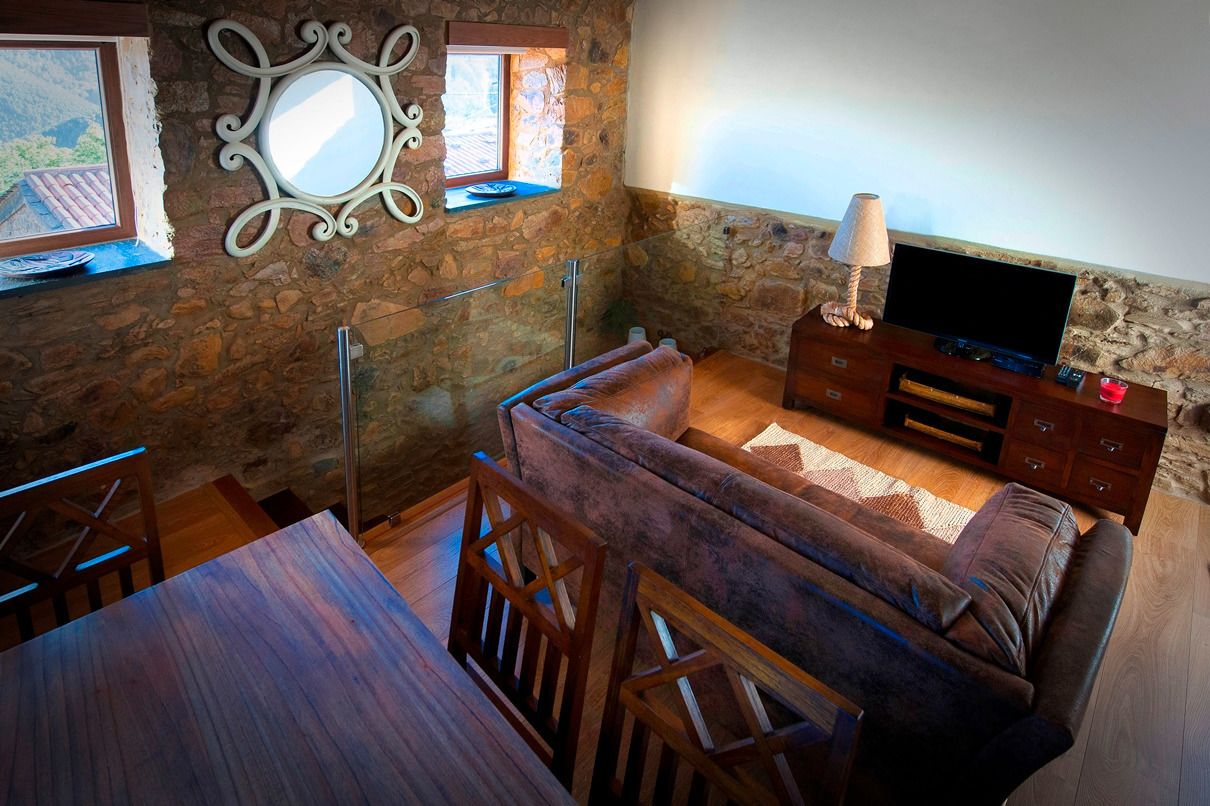 Una sala de estar acogedora con una pared de piedra, un sofá, un televisor y un comedor con una mesa y sillas.