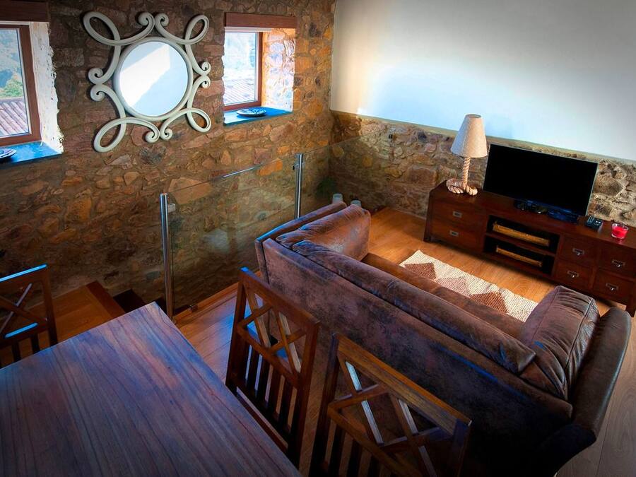 A cozy living room with a stone wall, a sofa, a TV, and a dining area with a table and chairs.