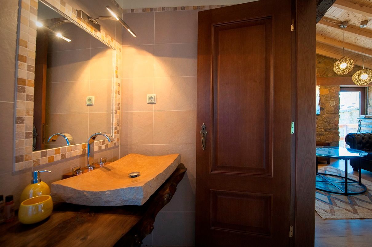Un bagno con lavabo in pietra, porta in legno e specchio illuminato.