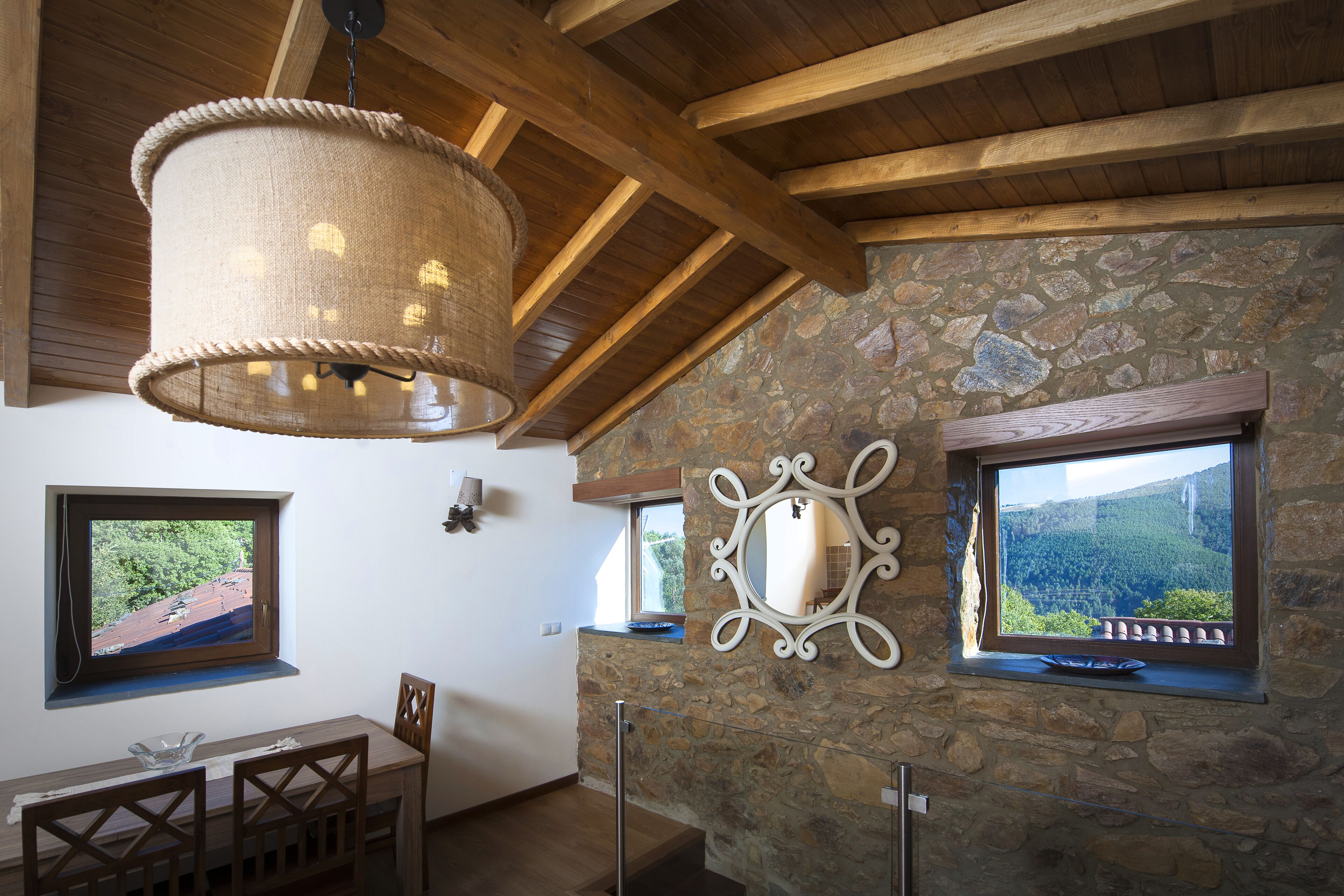 Un coin repas avec une table et des chaises en bois, un mur en pierre et une vue par la fenêtre.
