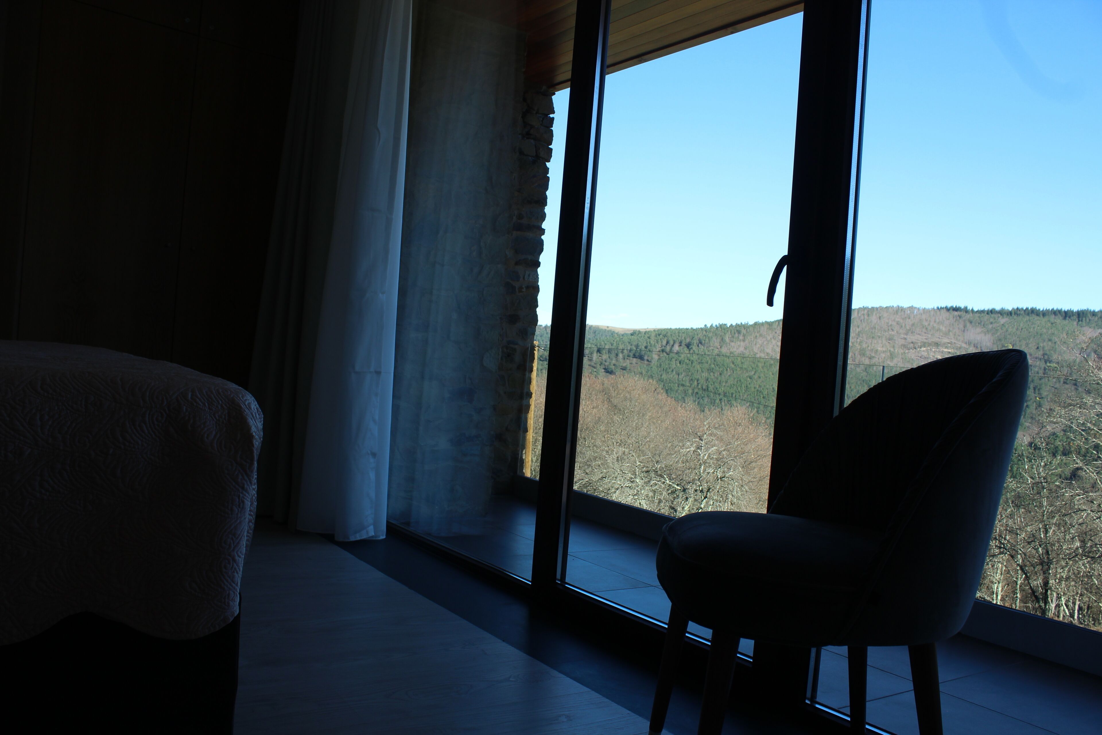 A room with a large window, a chair, and a bed.