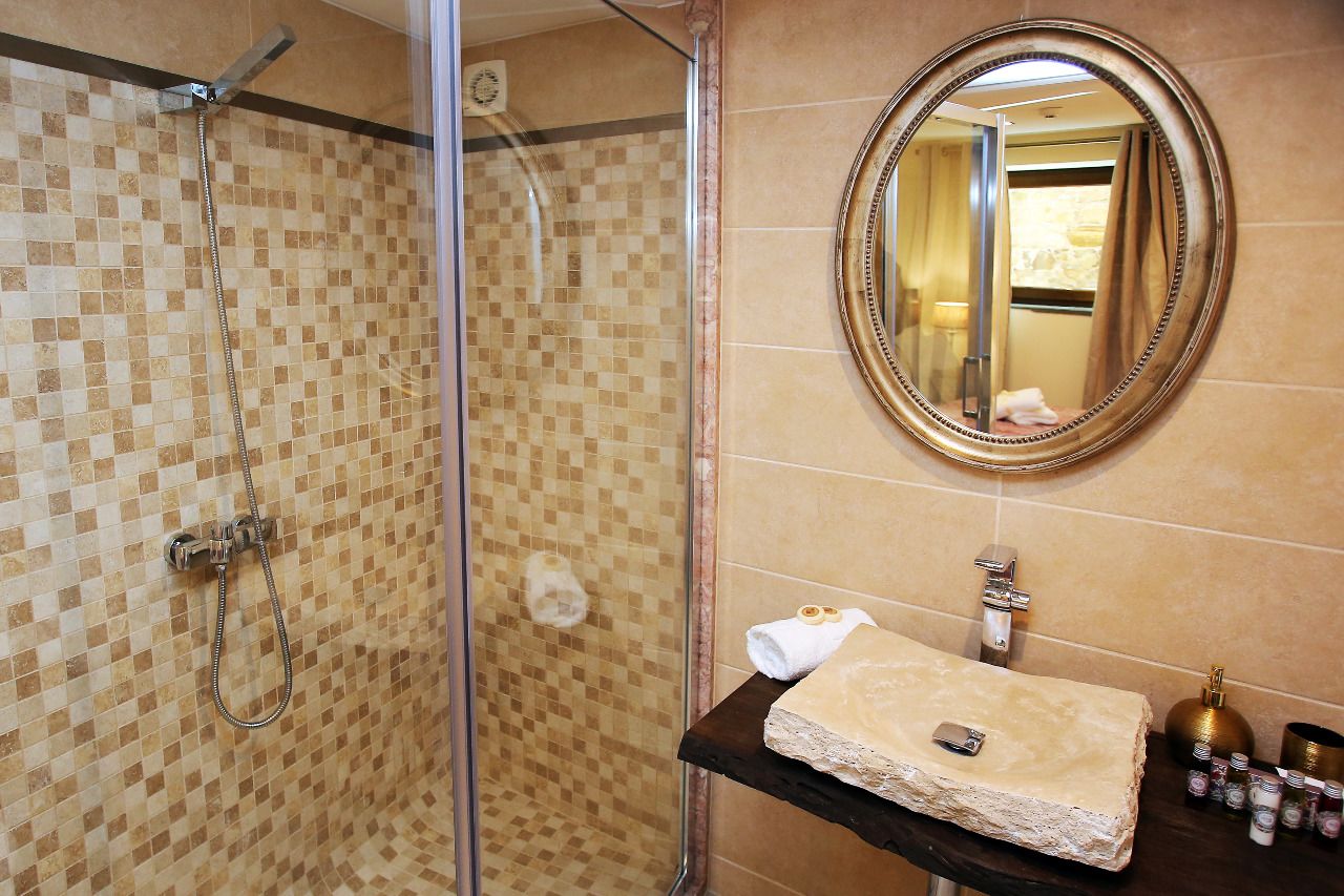 A bathroom with a glass-enclosed shower, a sink with a stone countertop, and a mirror with a gold frame.