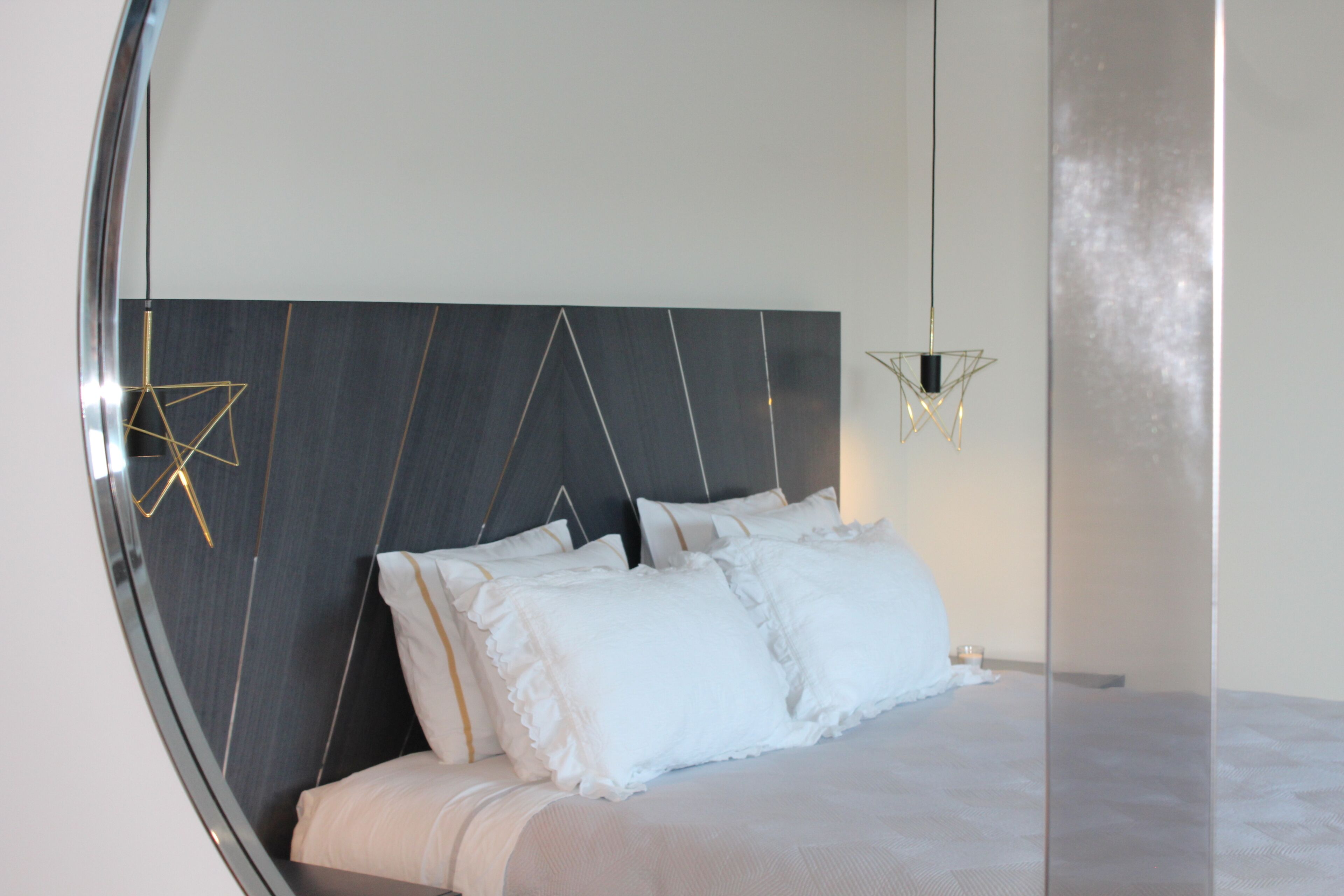 A modern bedroom with a dark headboard, white bedding, and a unique geometric light fixture.