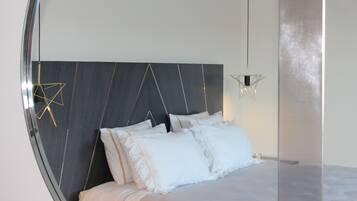 A modern bedroom with a dark headboard, white bedding, and a unique geometric light fixture.