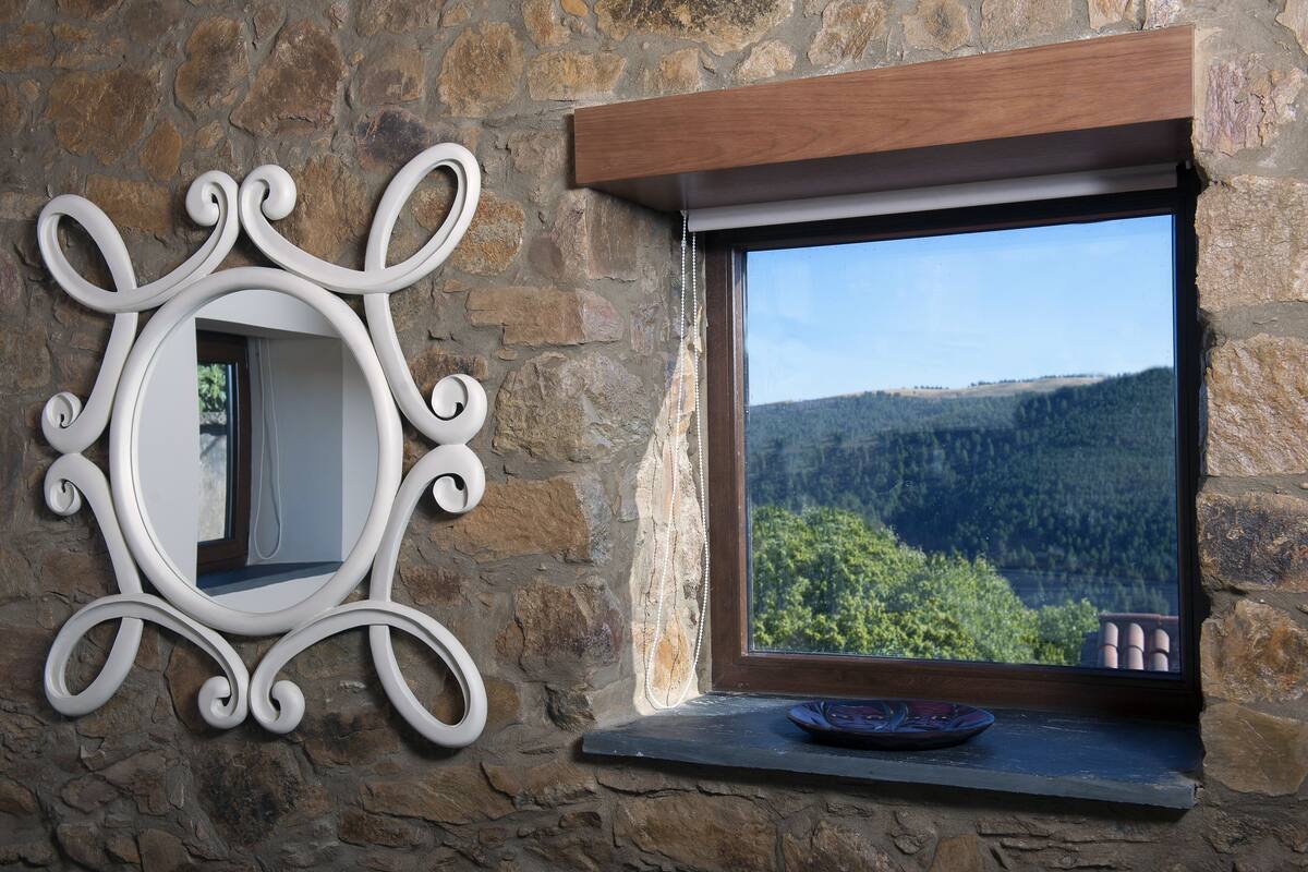 A stone wall with a decorative mirror and a window with a view of a forested landscape.