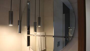 A modern bathroom with a large mirror, three pendant lights, and a towel hanging on the wall.