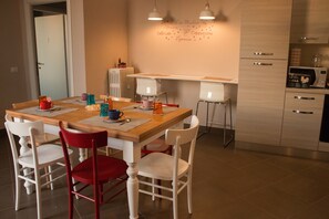 A dining area with a wooden table, white chairs, and a kitchen area with a microwave and cabinets. - La Terrazza di Evelina Guest House (Rome)