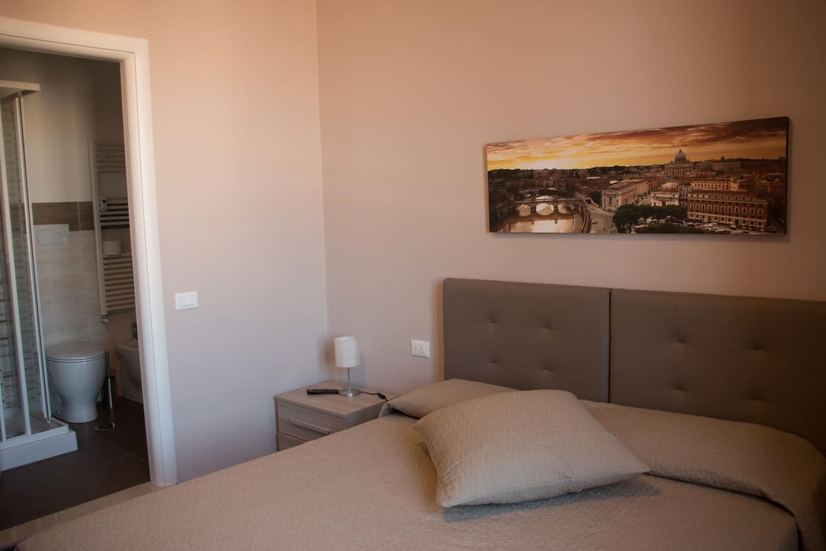A bedroom with a bed, a nightstand, a lamp, and a painting of a cityscape.