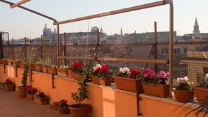 A rooftop terrace with terracotta planters arranged in a row, overlooking a cityscape with historic buildings and a prominent church spire.