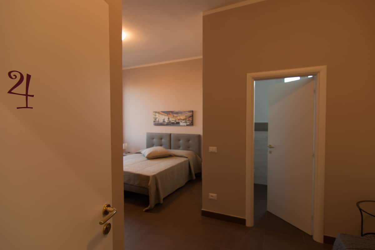 A bedroom with a bed, a headboard, a painting on the wall, and a door with the number 4.