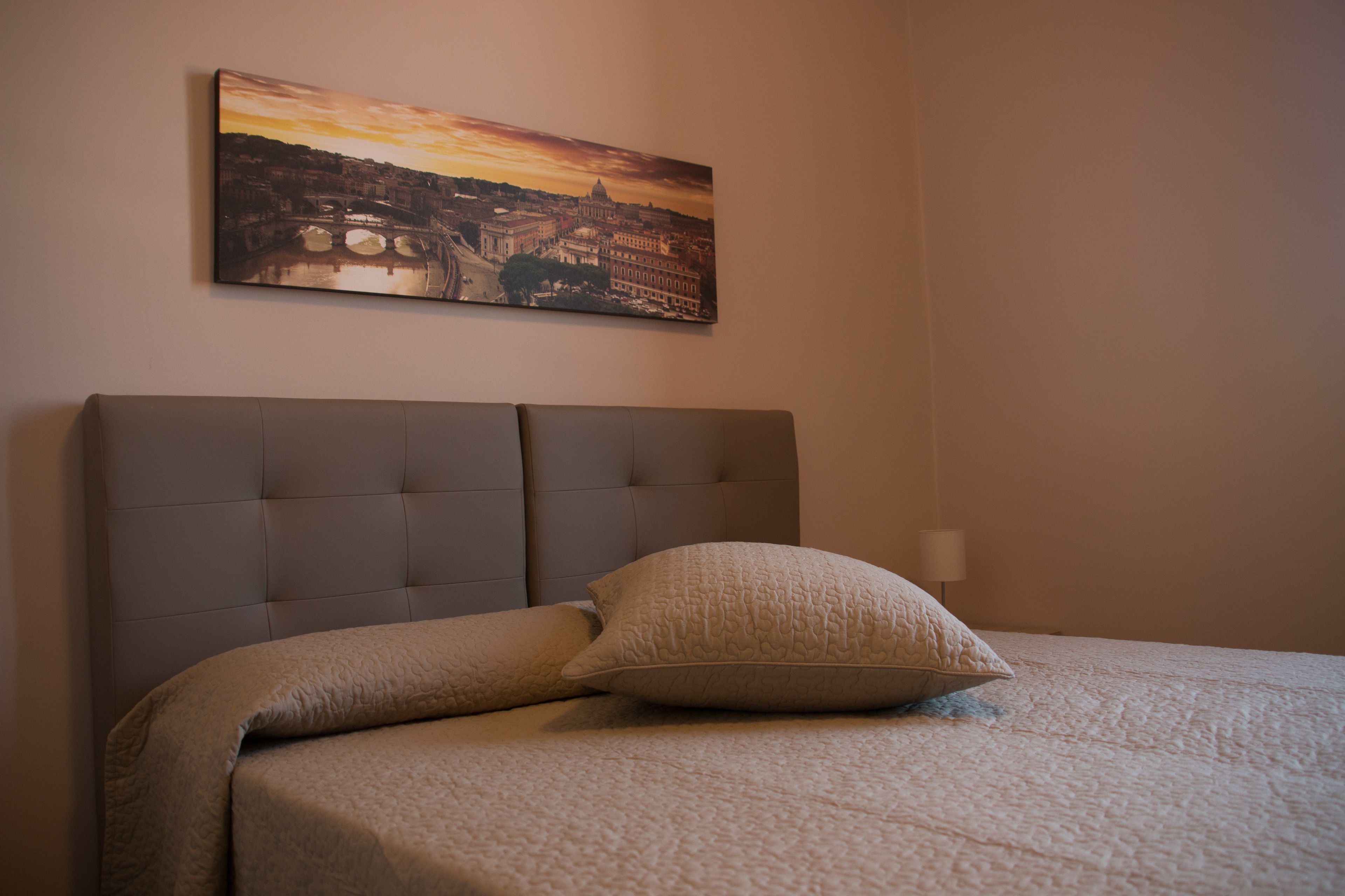 A bedroom with a large bed, a headboard, and a painting of a cityscape on the wall.