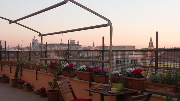 A rooftop terrace with a wooden pergola, potted plants, and a table with chairs.