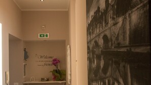 A hallway with a welcome sign, a framed cityscape, and a suitcase on the floor.