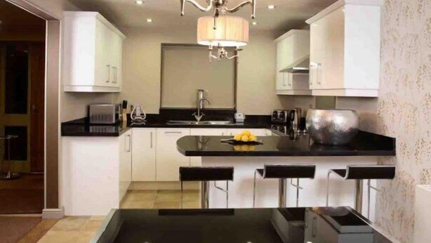Una cocina moderna con armarios blancos, encimera negra y una isla central con taburetes de bar.