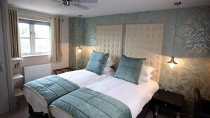 Una cama doble con cabecera capitonada, dos mesitas de noche, un ventilador de techo y una ventana con cortinas.