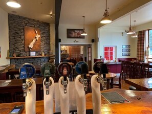 A bar area with multiple taps, a stone wall, and a view of the restaurant in the background.