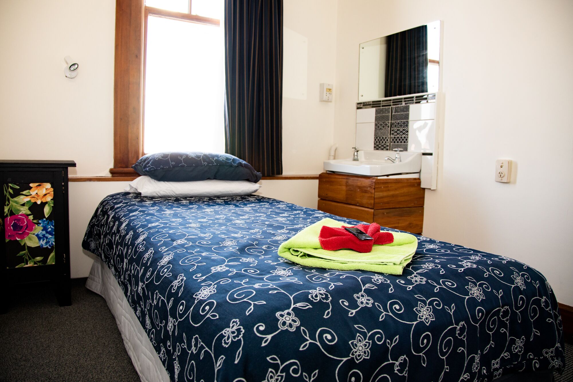 A bedroom with a bed, a dresser, a mirror, and a window with curtains.