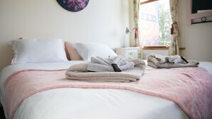 A neatly made bed with white and pink linens, a floral wall decoration, and a window with floral curtains. - The Brown Pub (Methven)