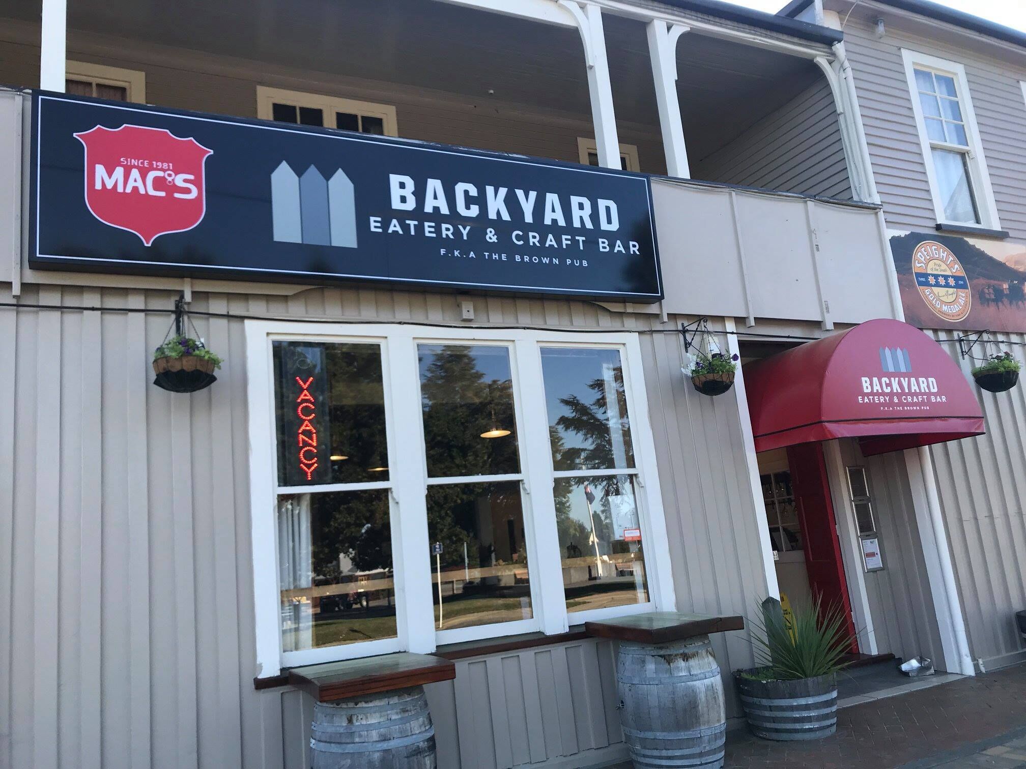 A storefront with a sign for Backyard Eatery & Craft Bar, a Mac's logo, and a vacant sign.