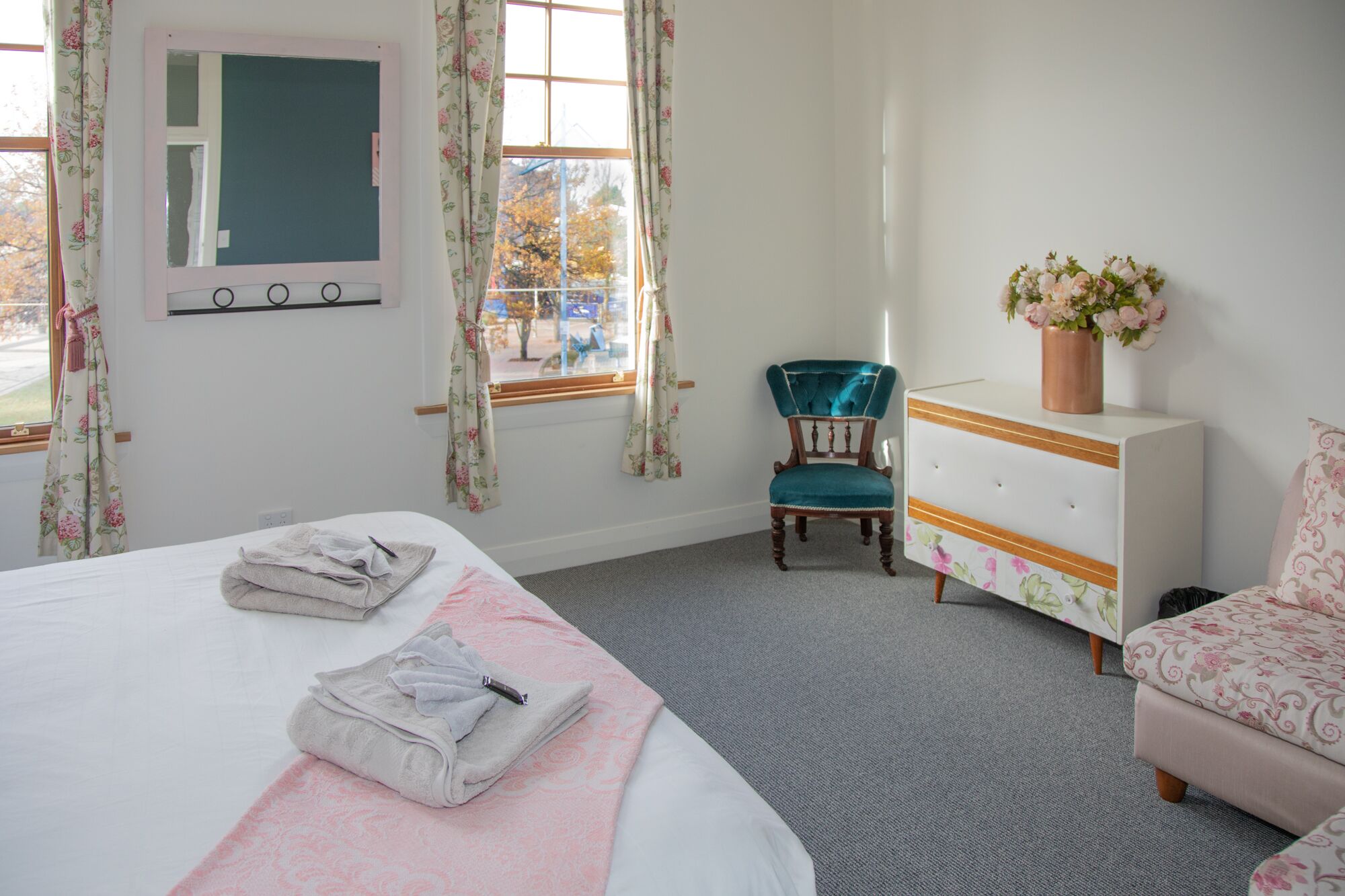 Un dormitorio con una cama, una silla, un aparador y una ventana con cortinas.