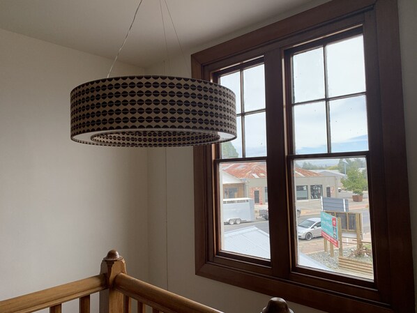 A room with a large window, a wooden railing, and a patterned hanging light fixture.