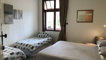 Een kamer met twee eenpersoonsbedden, een groot raam met gordijnen, een spiegel en kunstwerken aan de wanden.