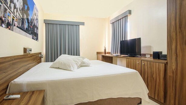 Una habitación de hotel con una cama, un escritorio con televisor y un armario de madera.