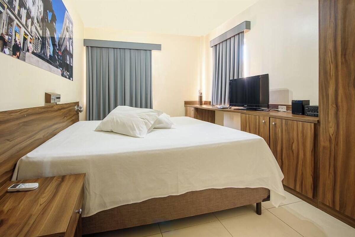 Una habitación de hotel con una cama, un escritorio con televisor y un armario de madera.