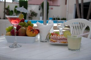 Une table avec un verre à martini, un saladier de fruits, une assiette de charcuterie et un verre contenant une boisson.