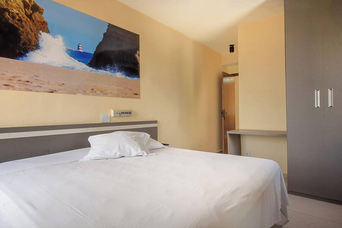 Una habitación de hotel con cama, un cuadro de una playa, un armario y una pequeña mesa.